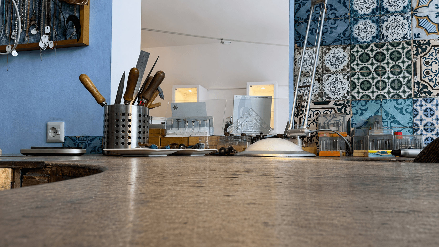 Werkbank der Goldwerkstatt Mondstein mit Werkzeug, Lampe und gemusterten Wandfliesen